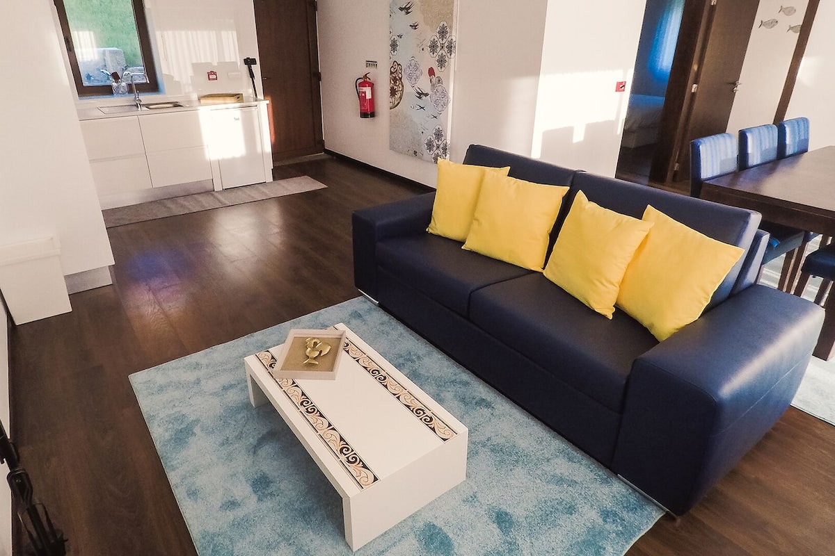 A modern living room with a dark blue sofa, yellow cushions, and a white coffee table with a decorative box.
