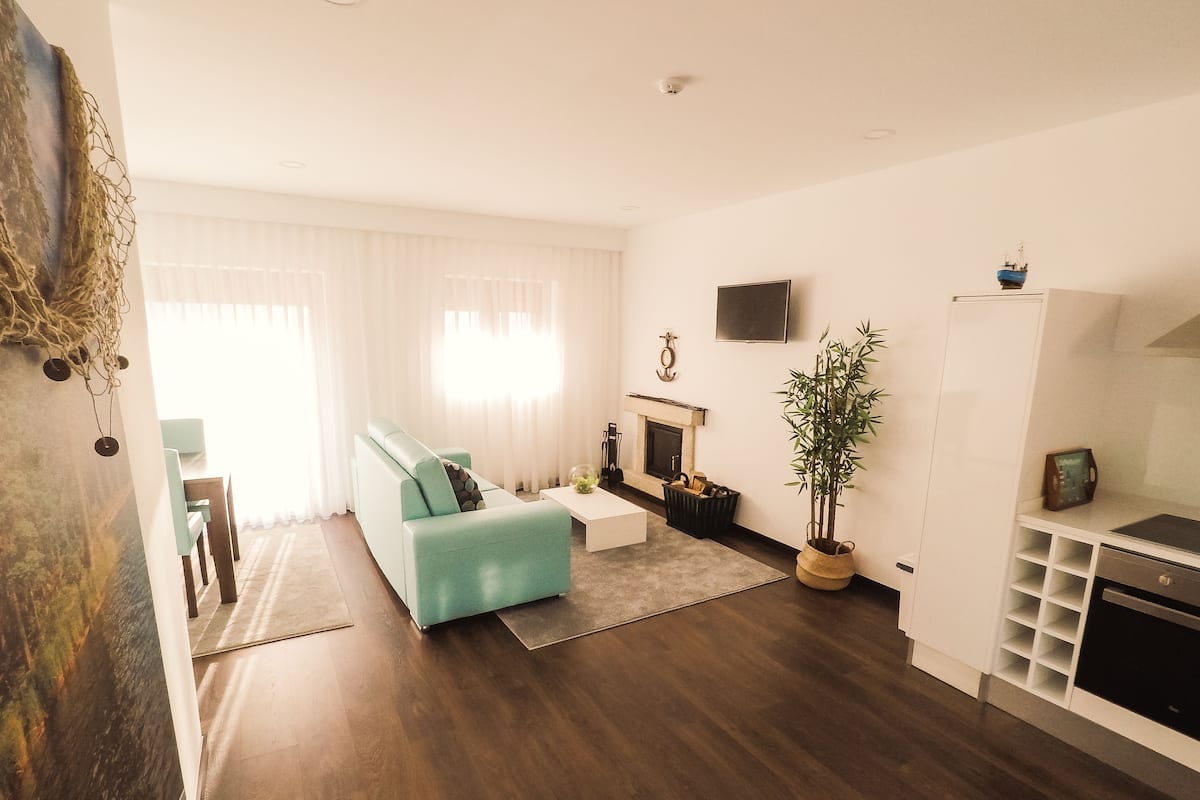 A modern living room with a teal sofa, a fireplace, a television, and a potted plant.