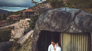 A couple standing in a stone-encased structure with a view of a winding road and distant houses.