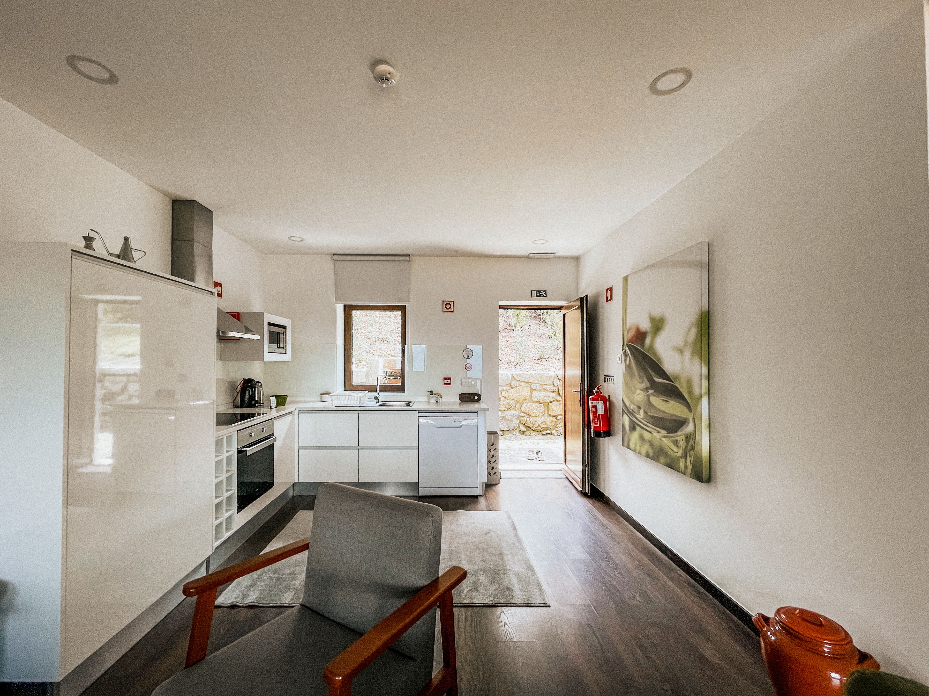 A modern kitchen with white cabinets, a built-in oven, and a microwave. There is a dining area with a chair and a table.