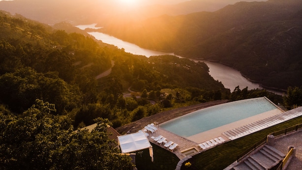 A resort with a swimming pool, surrounded by lush greenery and a view of a river.