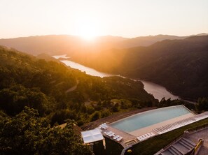 A resort with a swimming pool, surrounded by lush greenery and a view of a river. - Pousadela Village (Vieira do Minho)