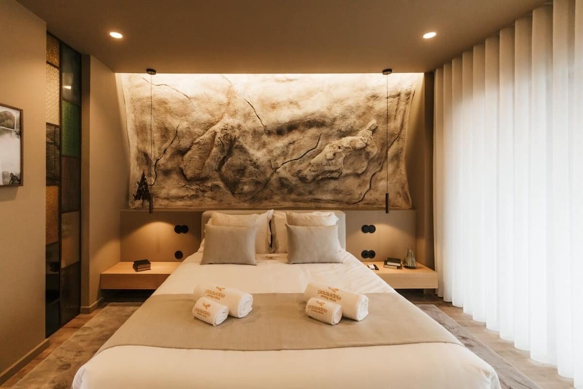 A hotel room with a large bed, two bedside tables, a wall-mounted artwork, and a window with curtains.