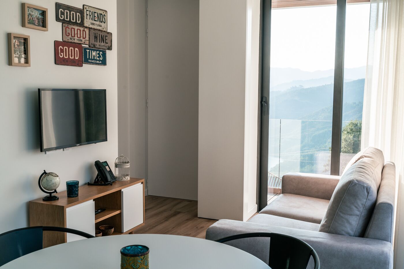 A modern living room with a TV, a wooden console table, a globe, and a sofa with a view of mountains.
