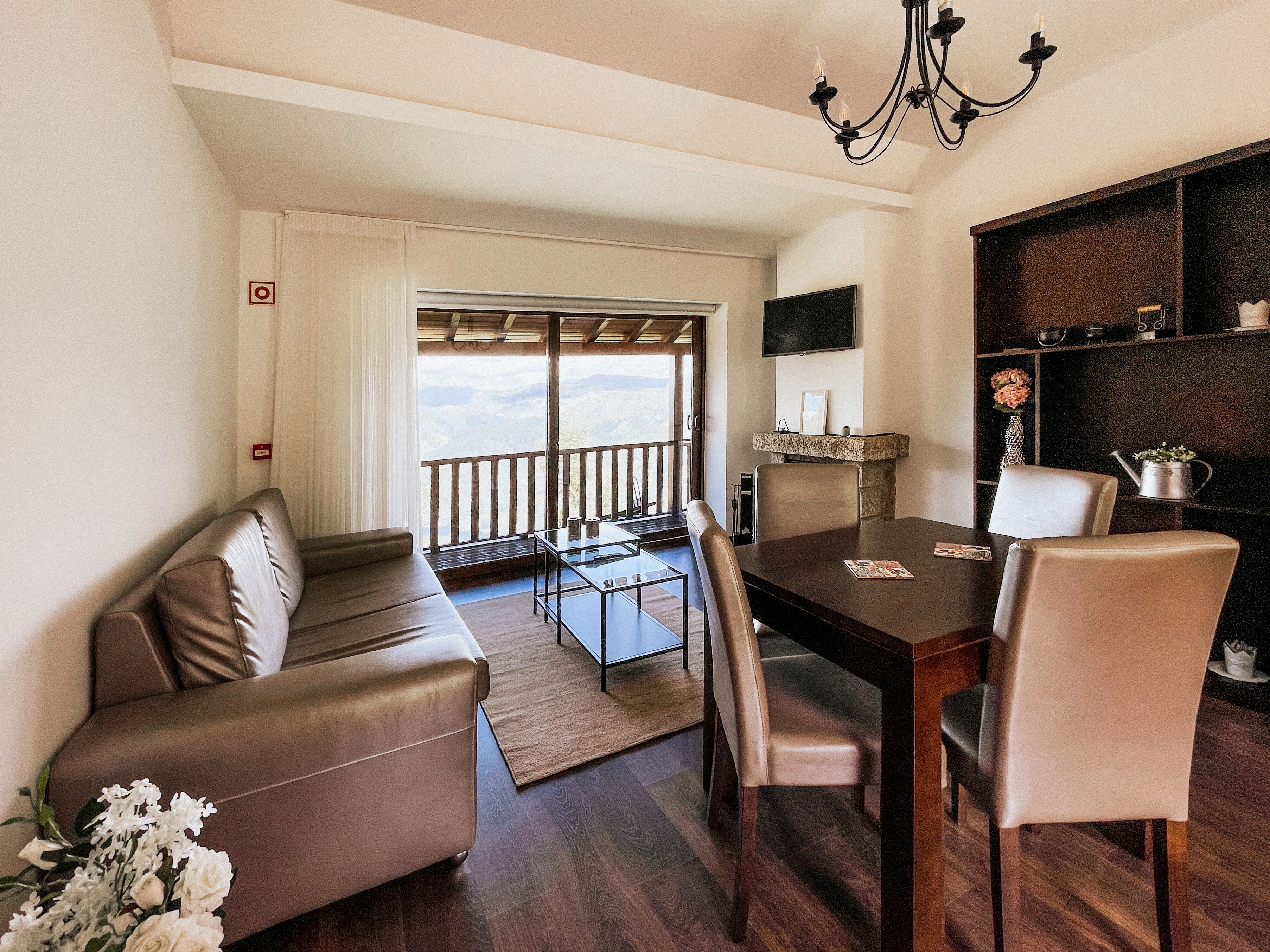 A modern living room with a dining area, a sofa, a table, and a balcony with a view.