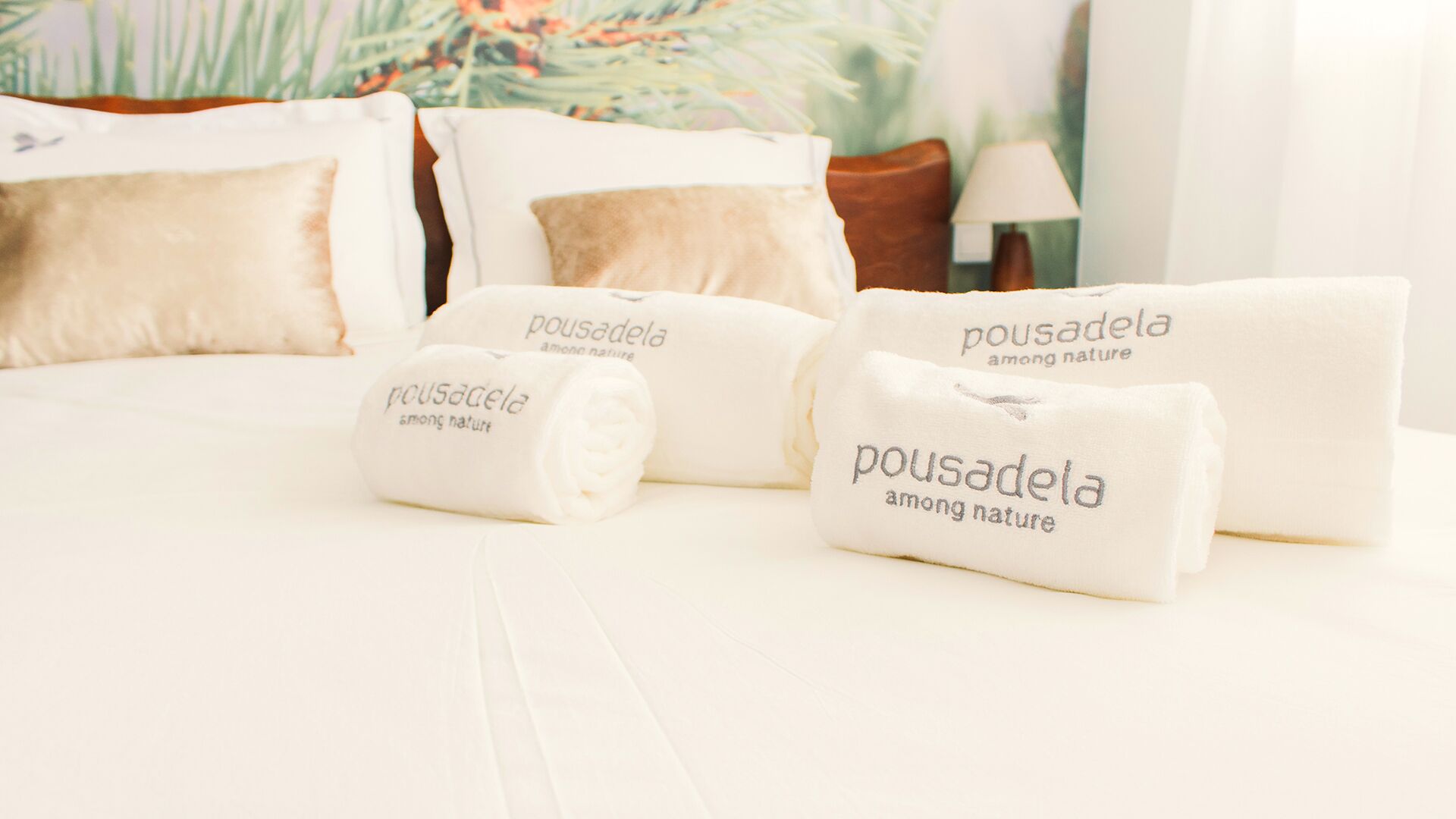 A neatly made bed with white bedding and pillows labeled 'pousadela among nature'.