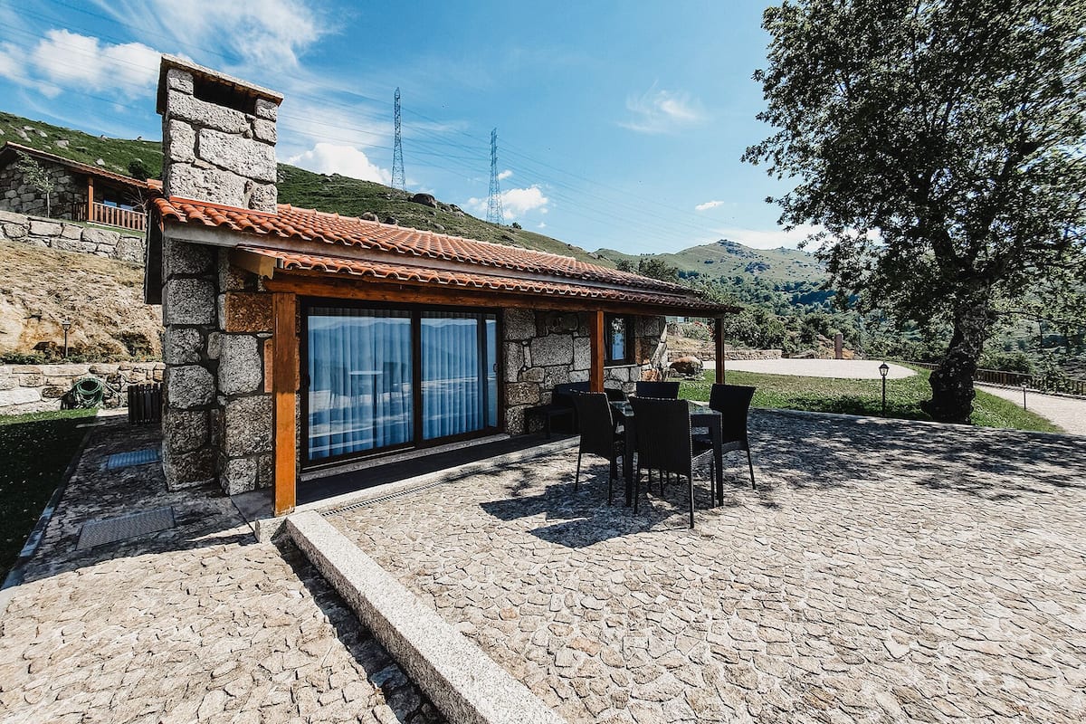 A stone building with a tiled roof, a glass door, and a patio with outdoor furniture.