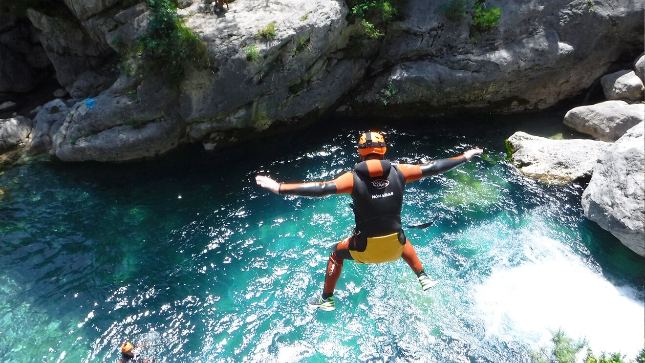A person jumping into a clear blue pool surrounded by rocky terrain.
