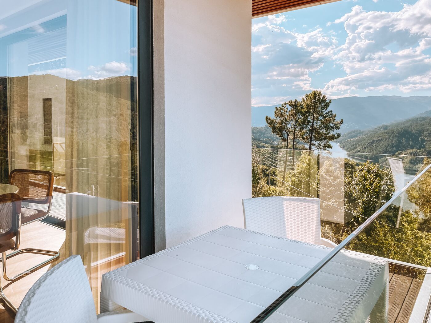 Un balcón con mesa y sillas, con vistas a un paisaje montañoso y un río.