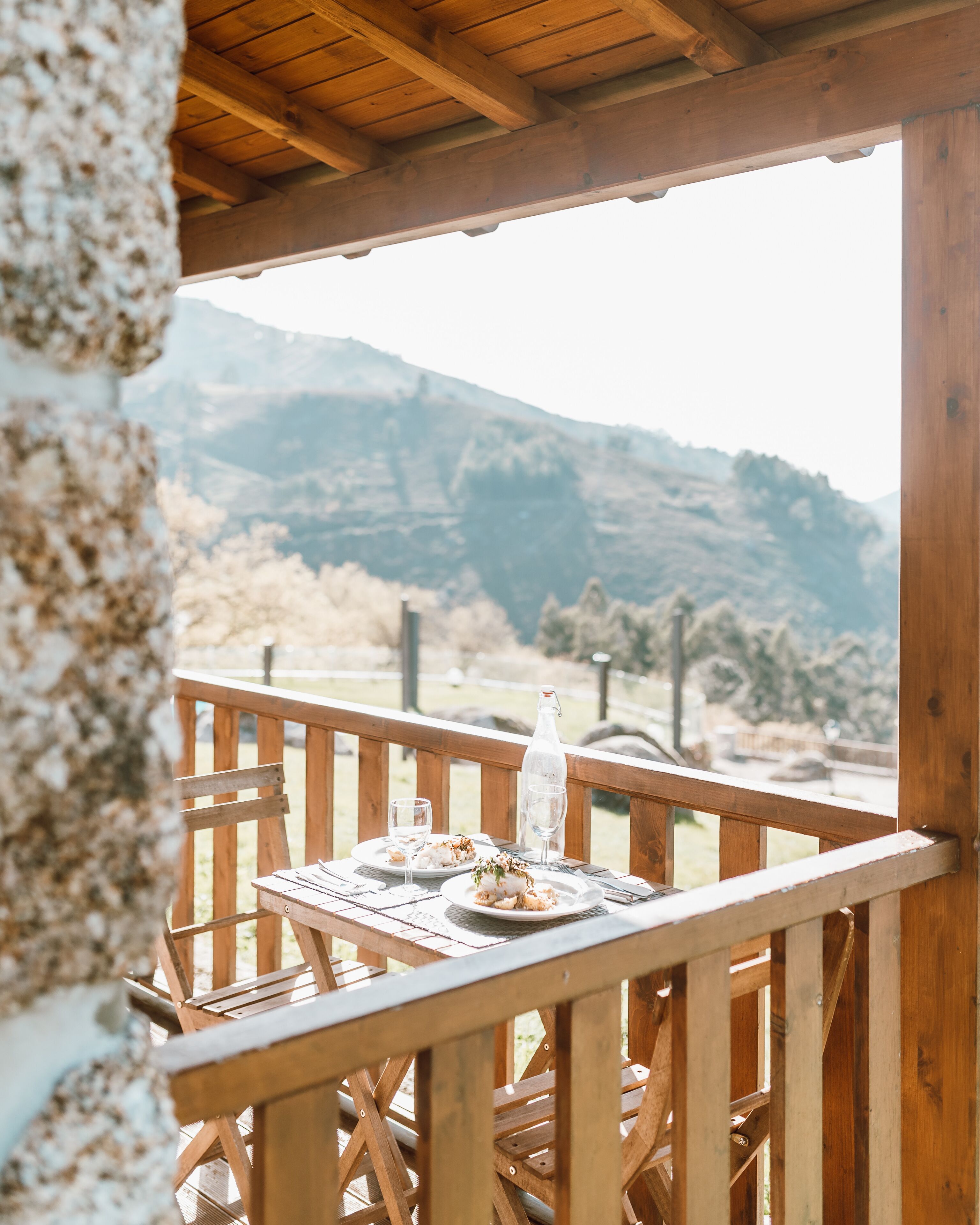 Una terraza de madera con una mesa dispuesta para dos, con vistas a un paisaje montañoso.