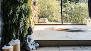 A modern interior with a large window, a stone Buddha statue, and a wall covered with ferns.