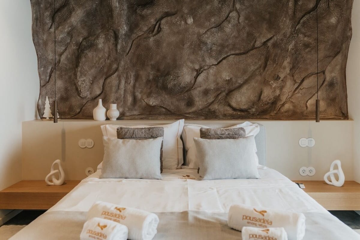 A hotel room with a large, textured wall headboard, a neatly made bed with white linens, and two bedside tables with decorative items.