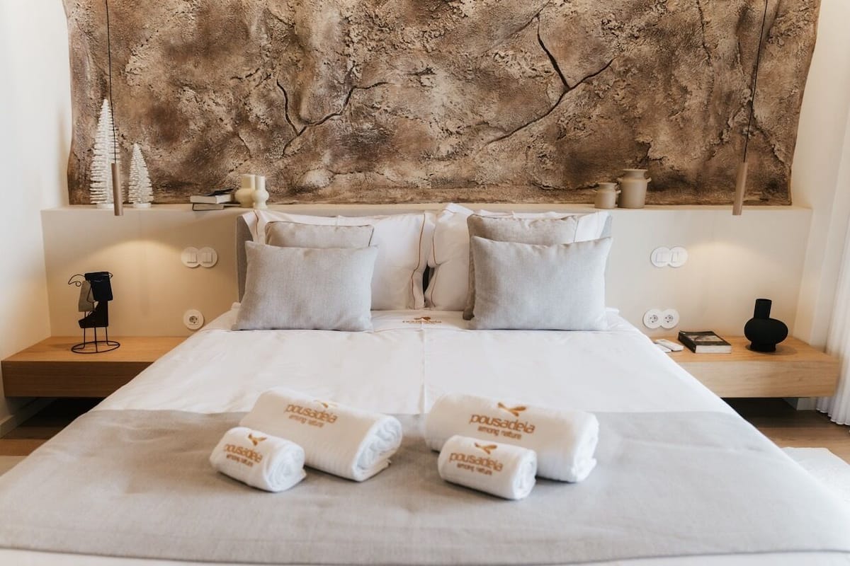 A hotel room with a large bed, two bedside tables, a wall art piece, and towels with a logo.