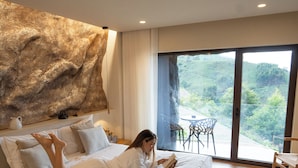 A modern bedroom with a large bed, a view of the outdoors, and a wooden floor.