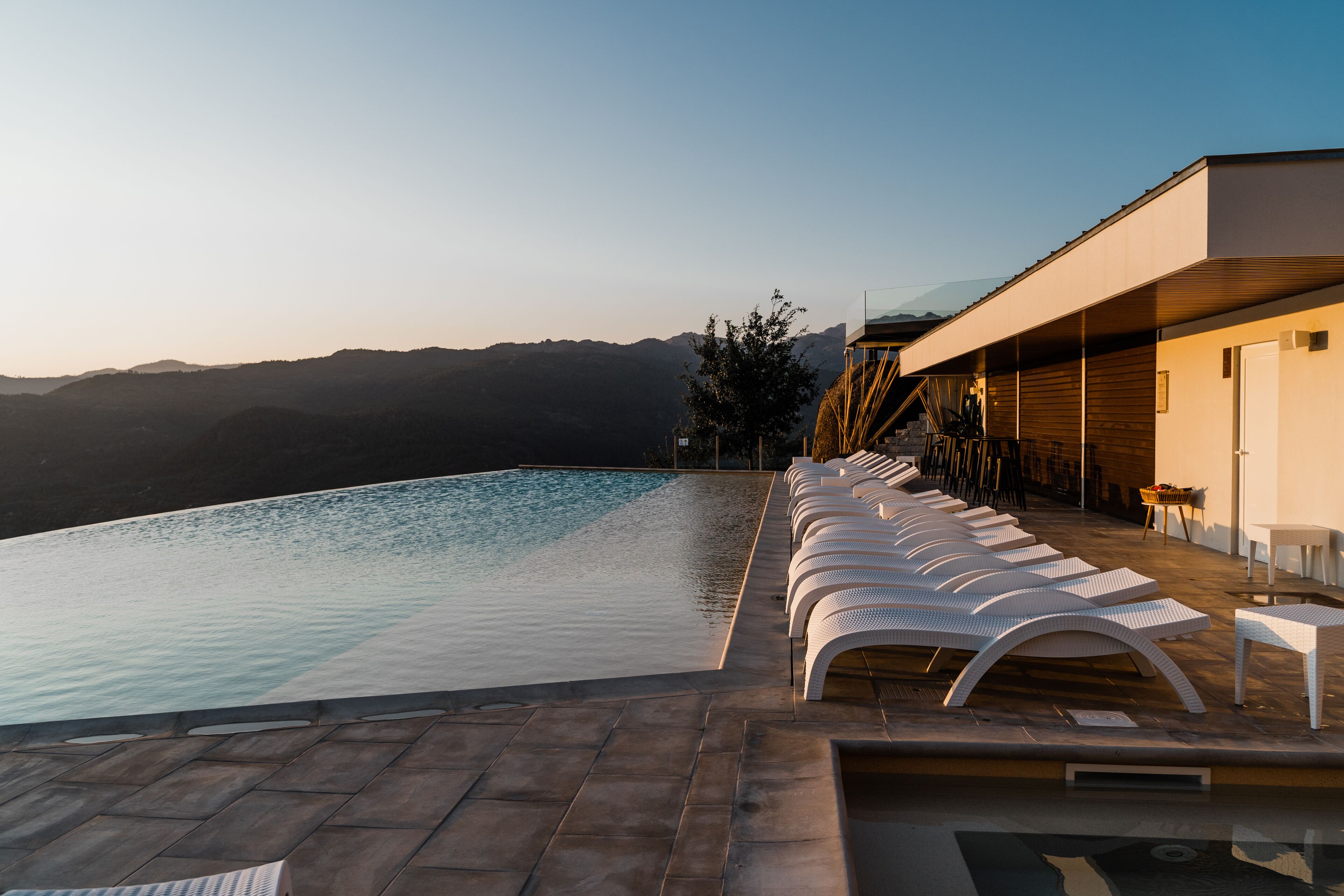 An infinity pool with lounge chairs, a wooden deck, and a mountain view.