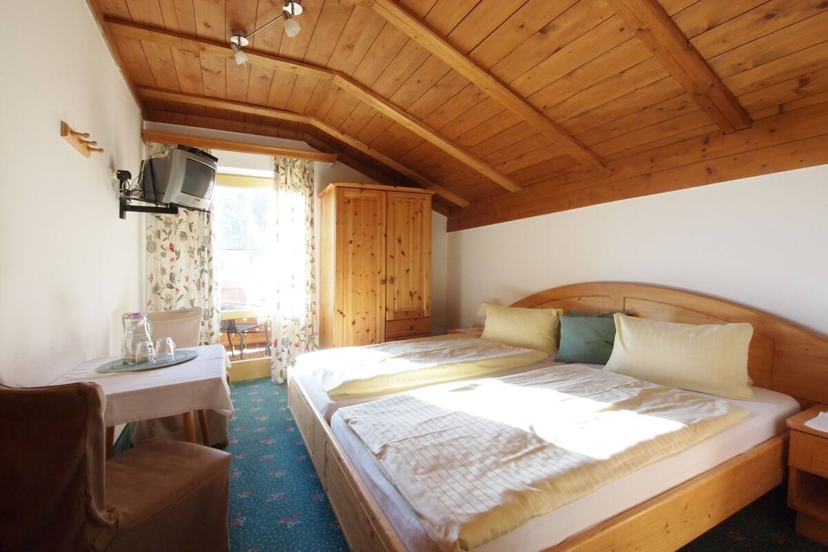 Quarto com painéis de madeira, uma cama, uma escrivaninha e uma cadeira.