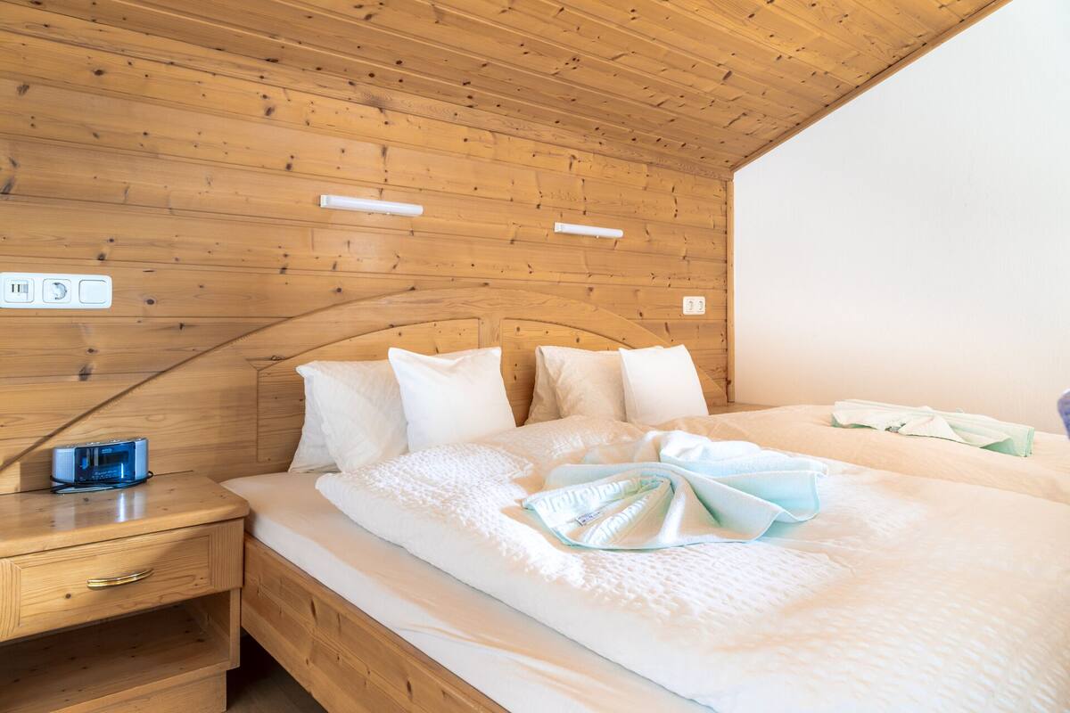 Quarto com painéis de madeira, uma cama, uma mesa de cabeceira e uma tomada.