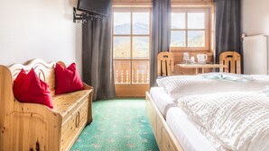 A room with a bed, a wooden bench with red pillows, a small table with a cup and a book, and a TV mounted on the wall. - Gasthof Pesbichl (Goldegg)