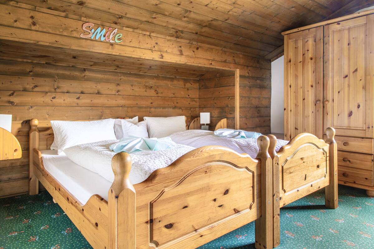 Uma cama de madeira com cabeceira, um guarda-roupa e uma parede com um letreiro que diz 'Smile'.