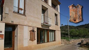 Een gebouw met twee verdiepingen, met een beige gevel, nummer 15, met een balkon met metalen hekwerk en een raam met gordijn.