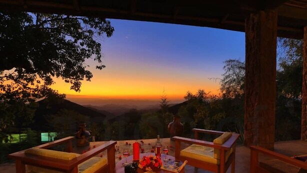 A sunset view from a covered outdoor seating area with wooden furniture and a table set for two. - Mezena Resort and Spa (Lalibela)