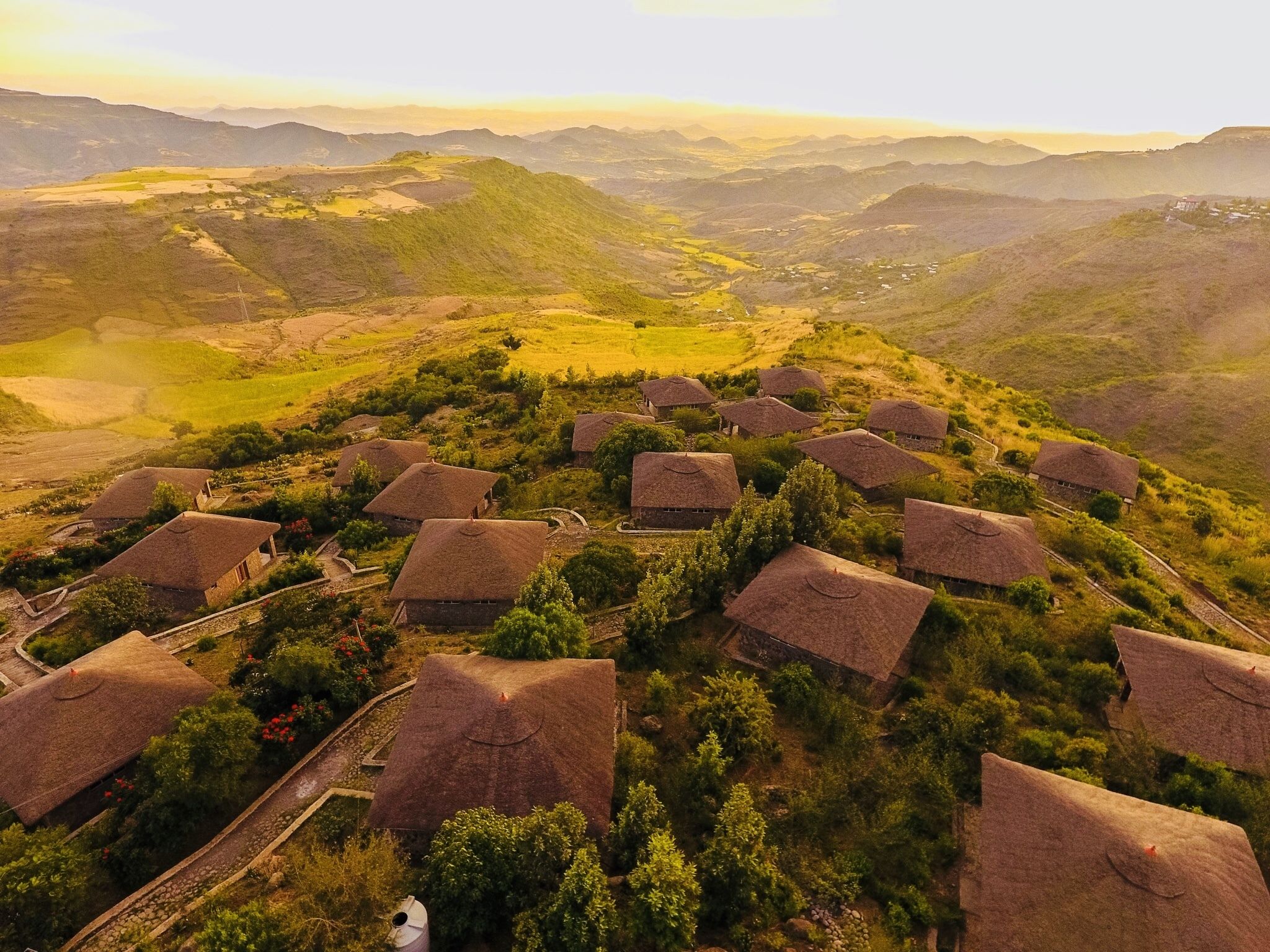 Un pueblo rural con casas de techo de paja agrupadas, rodeado de abundante vegetación y colinas ondulantes.