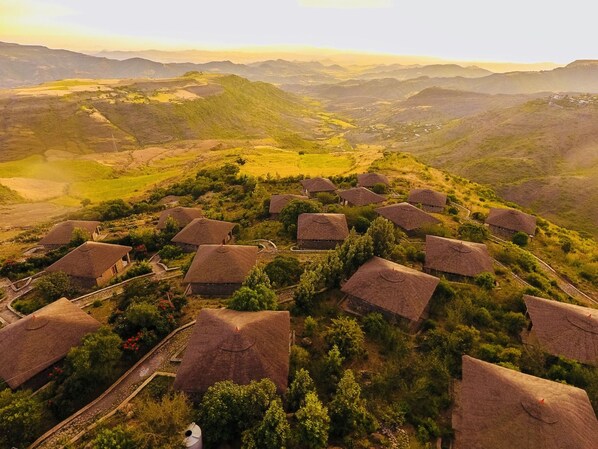 A rural village with thatched-roof houses clustered together, surrounded by lush greenery and rolling hills. - Mezena Resort and Spa (Lalibela)