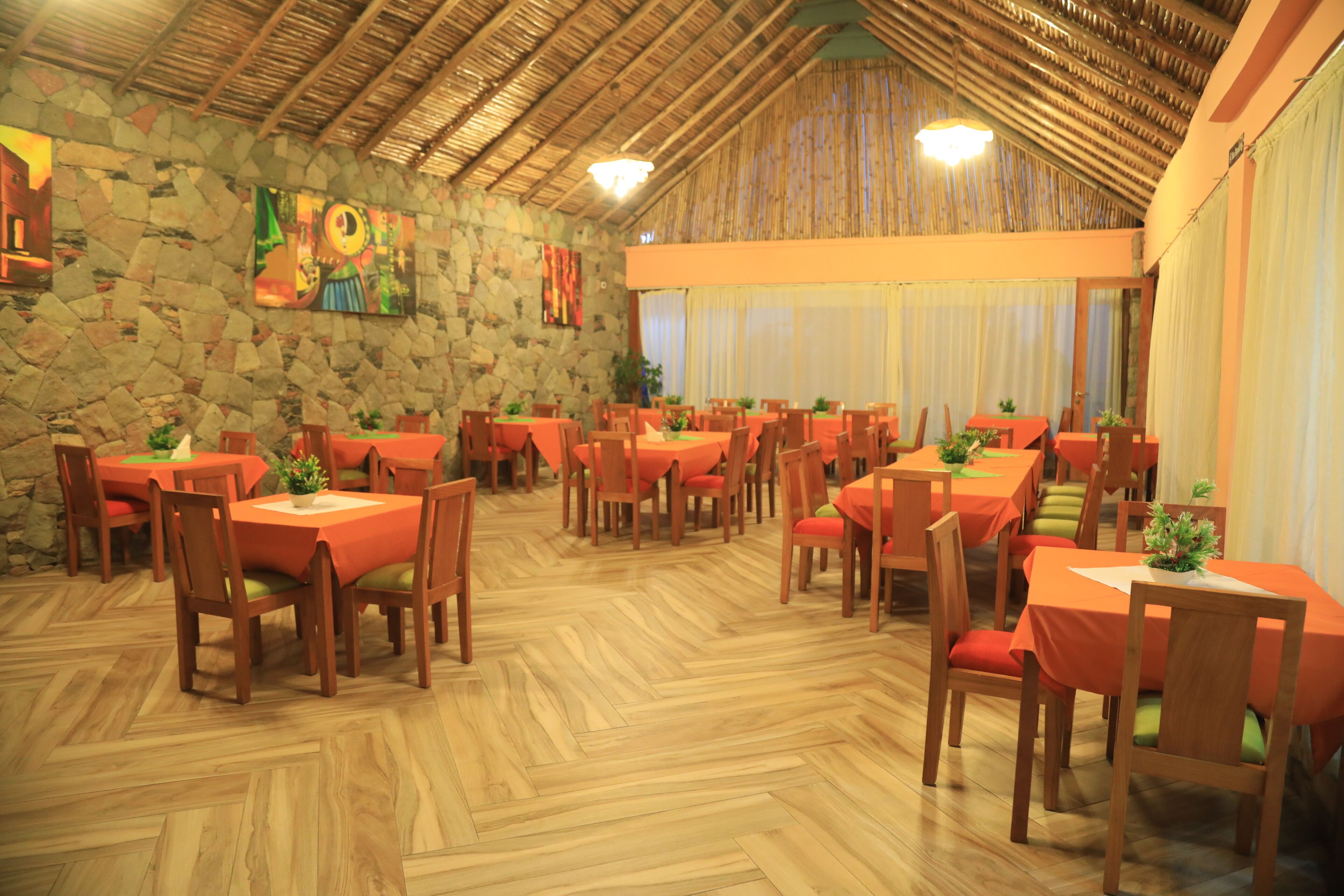 A restaurant with multiple tables and chairs, stone walls, and wooden flooring.