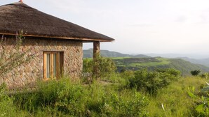 A stone building with a thatched roof, a wooden door, and a view of rolling hills in the background. - Mezena Resort and Spa (Lalibela)