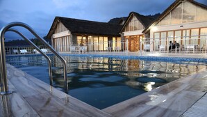 A swimming pool with a wooden deck, metal railings, and a building with large windows and a thatched roof in the background. - Mezena Resort and Spa (Lalibela)