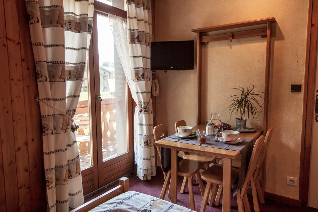 A wooden room with a dining table, chairs, a television mounted on the wall, and a window with curtains.