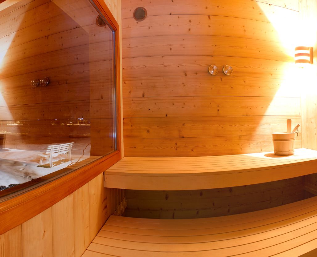 A wooden sauna with a bench, a window, and a small table with a bucket.