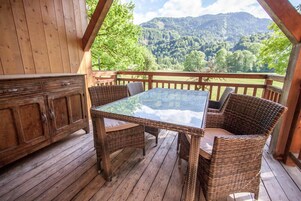 A wooden deck with wicker furniture and a glass table, overlooking a mountainous landscape.