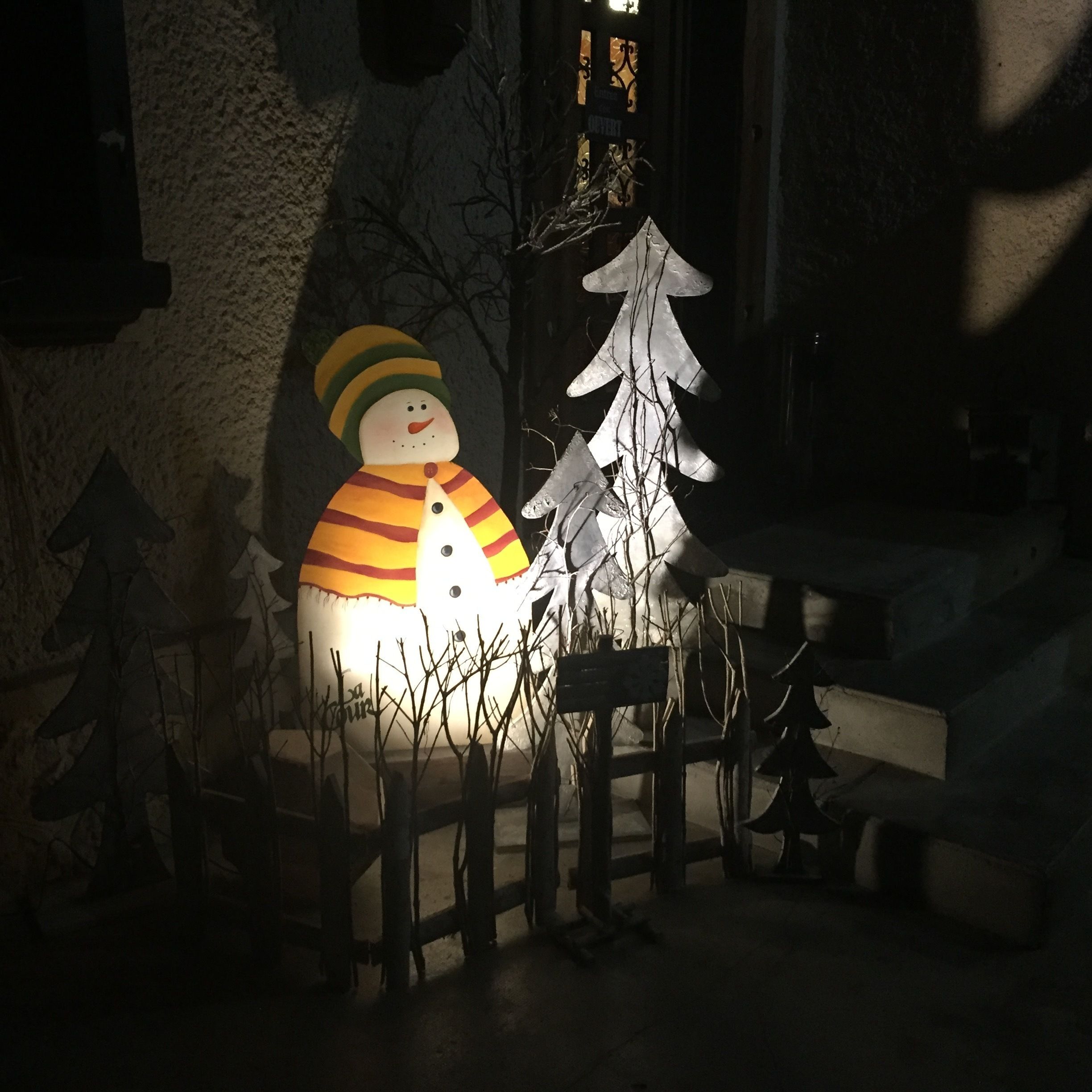 Una decoración de muñeco de nieve con un árbol a su lado, frente a una fachada de edificio.