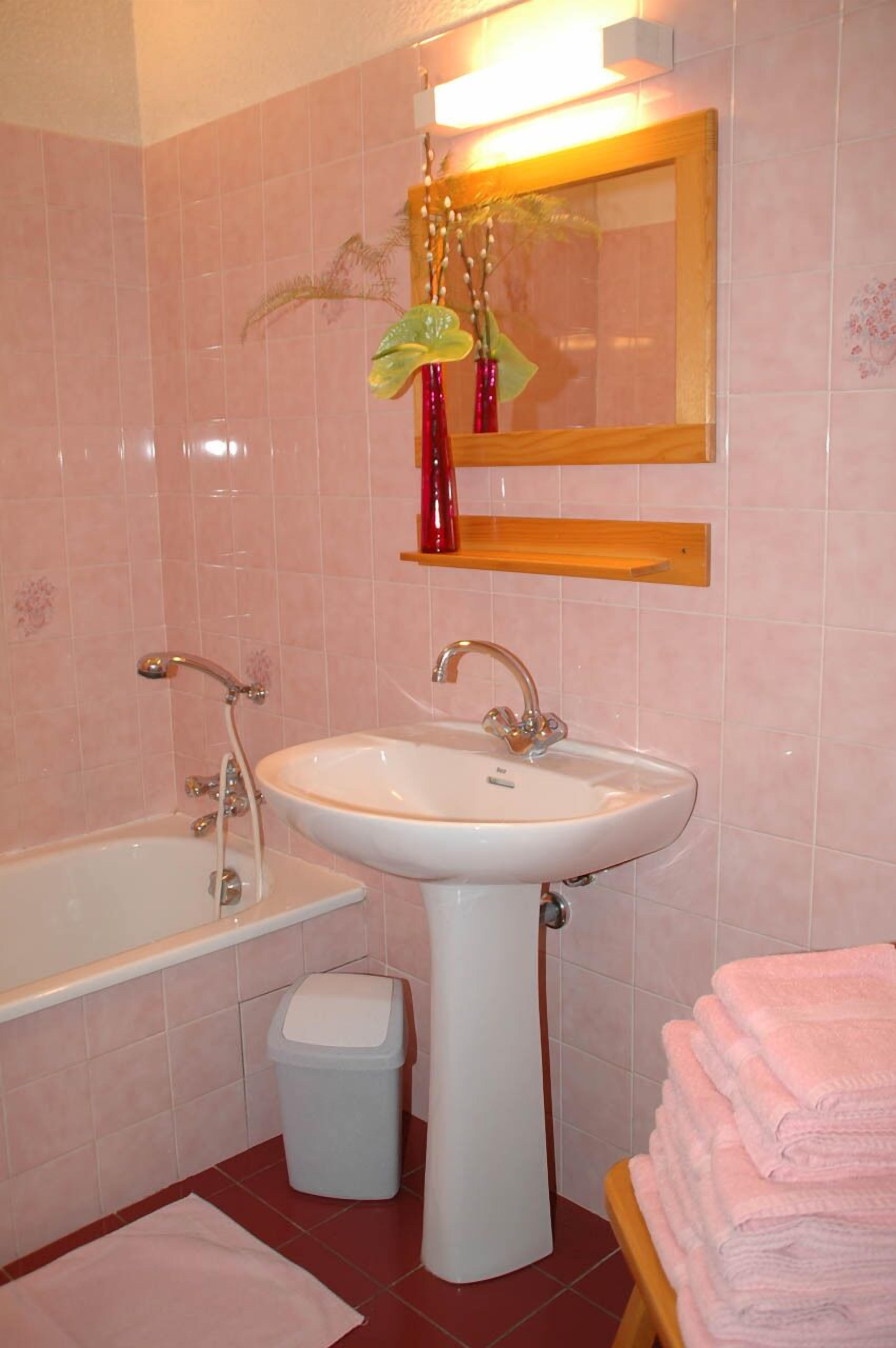 Un bagno con un lavandino bianco, una vasca, un cestino e una pila di asciugamani rosa.