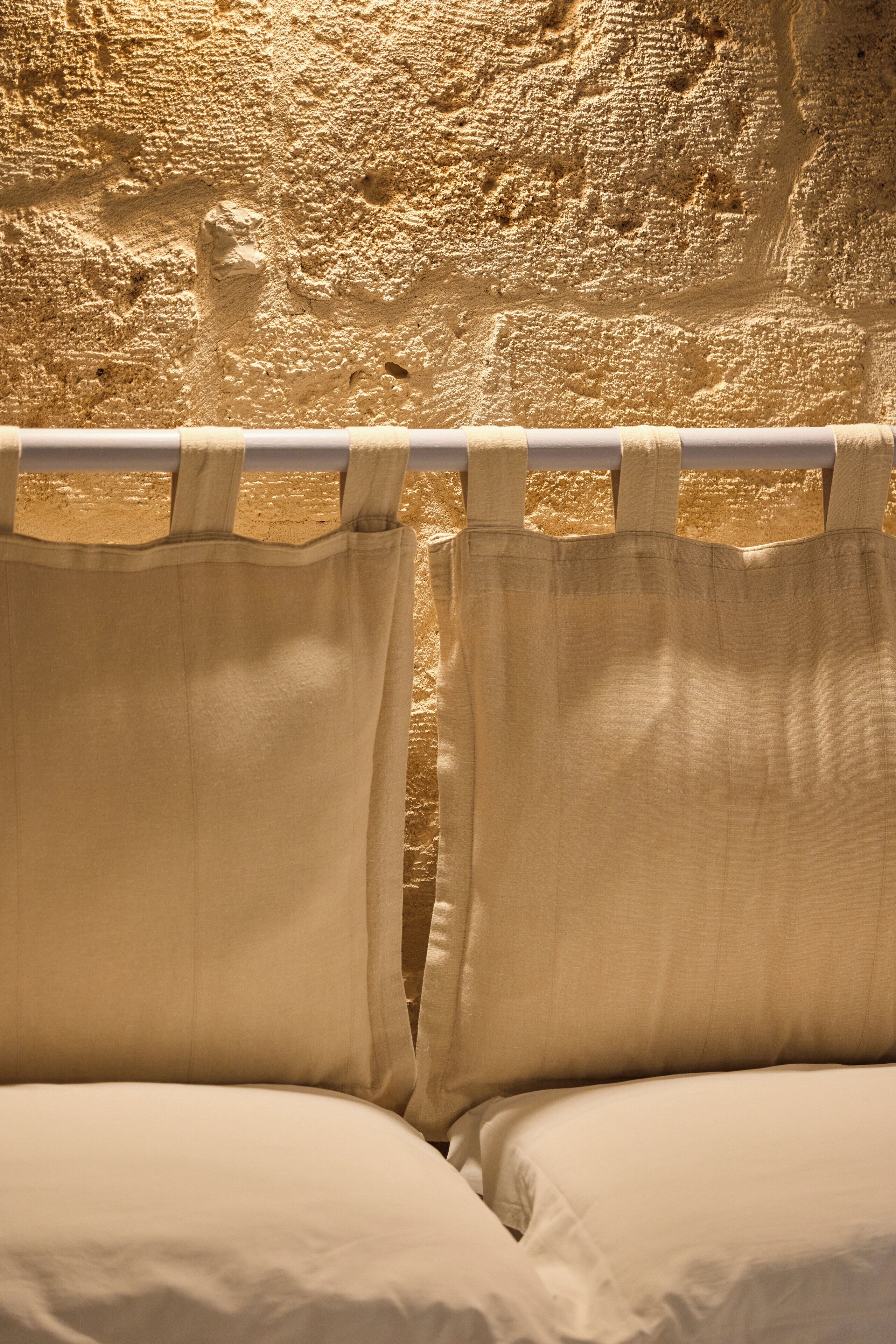 Un lit avec du linge de lit blanc et une tête de lit en bois, adossé à un mur à la texture particulière.