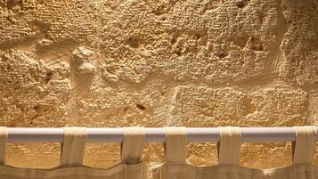 Un lit avec du linge de lit blanc et une tête de lit en bois, adossé à un mur à la texture particulière.