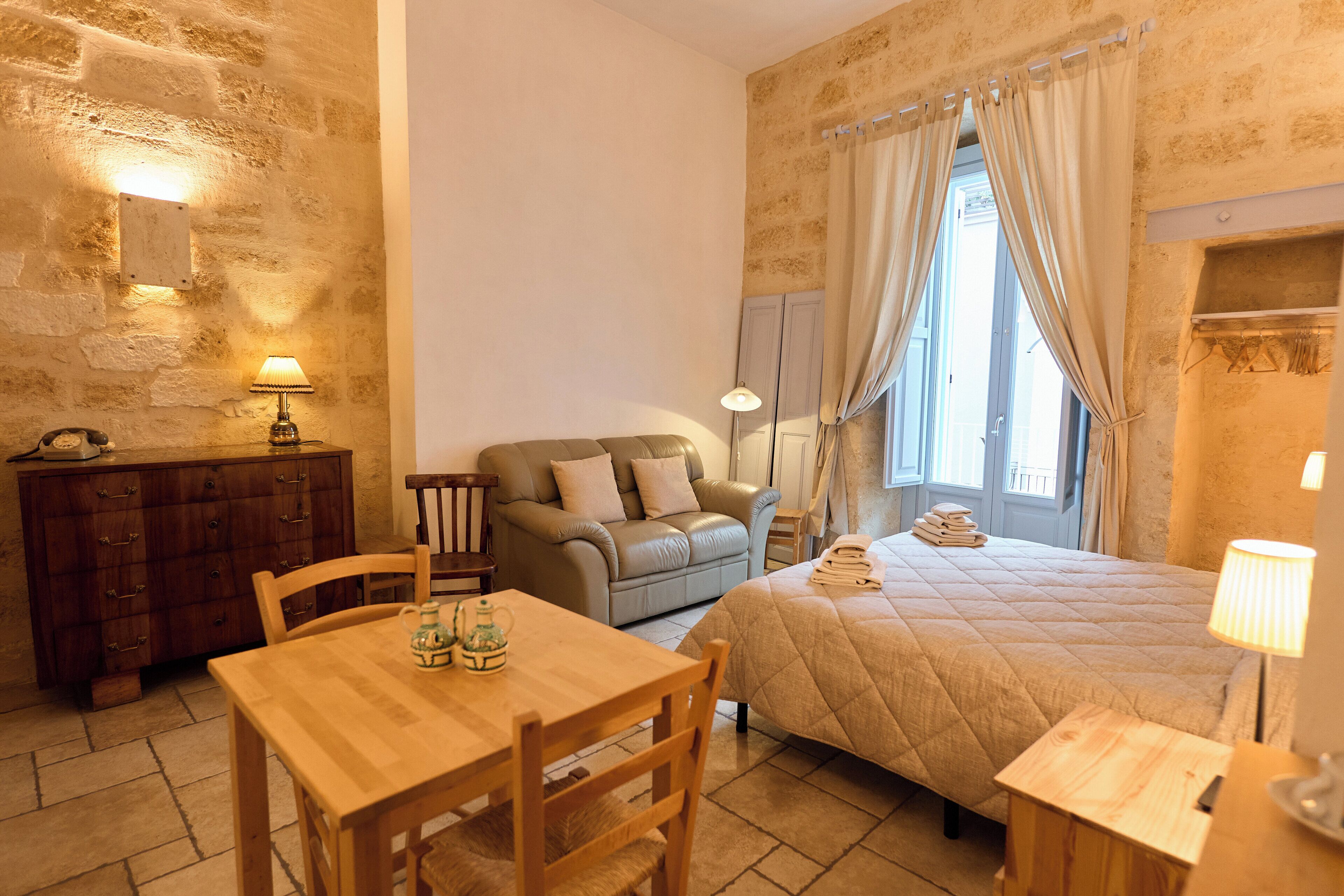 Una habitación acogedora con una mesa de madera, un sofá, una cama con colcha, un aparador y un espejo.