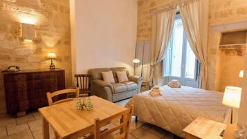 Una habitación acogedora con una mesa de madera, un sofá, una cama con colcha, un aparador y un espejo.