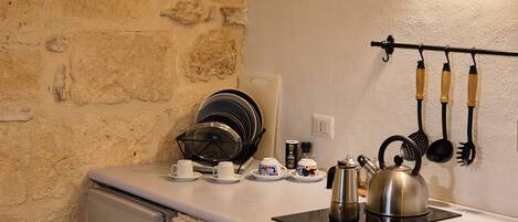 A compact kitchen with a stone wall, a small refrigerator, a kettle, and a utensil rack.