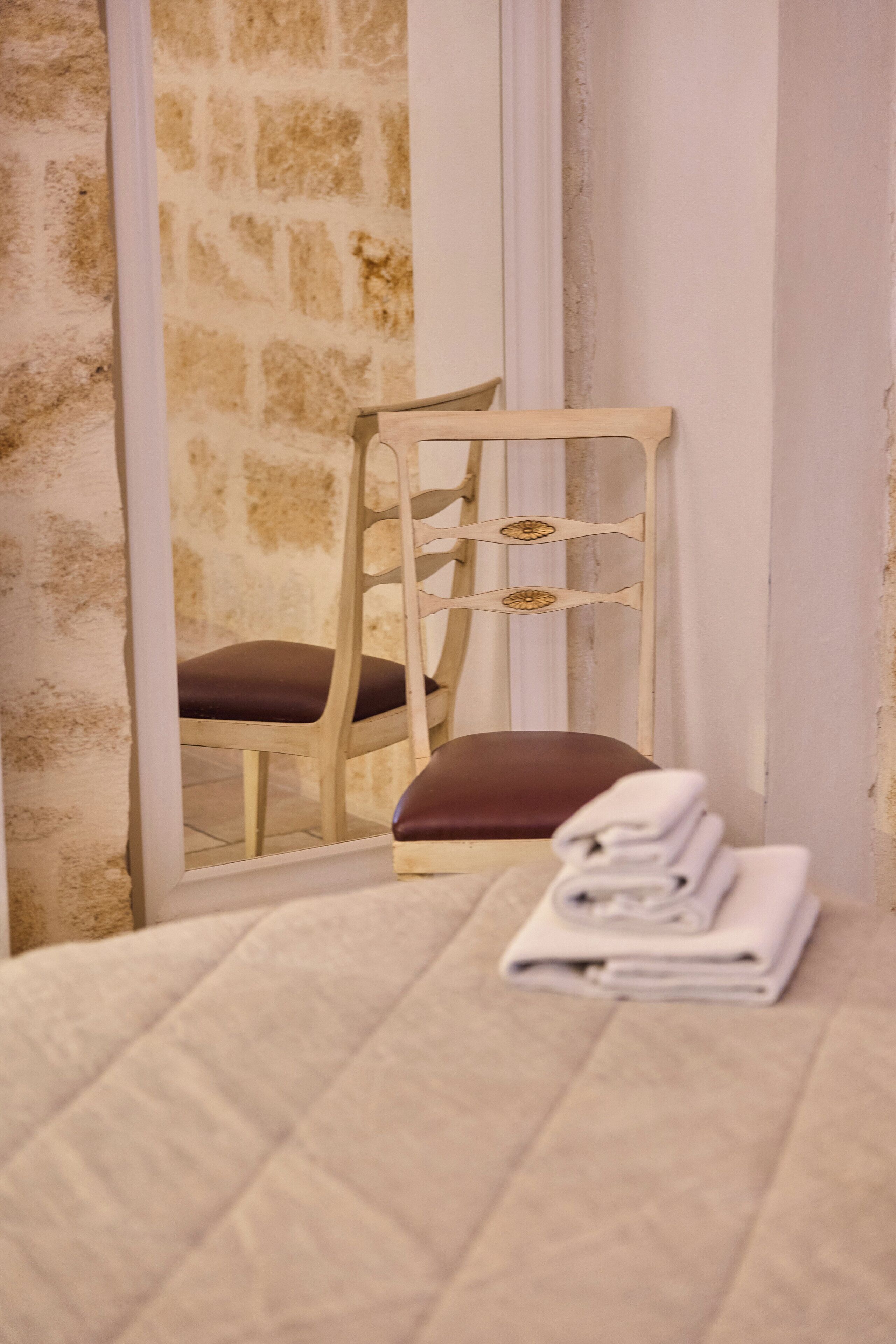 Ein Bett mit gesteppter Bettdecke, ein hölzerner Stuhl mit gepolstertem Sitz und ein gefaltetes Handtuch auf dem Boden.