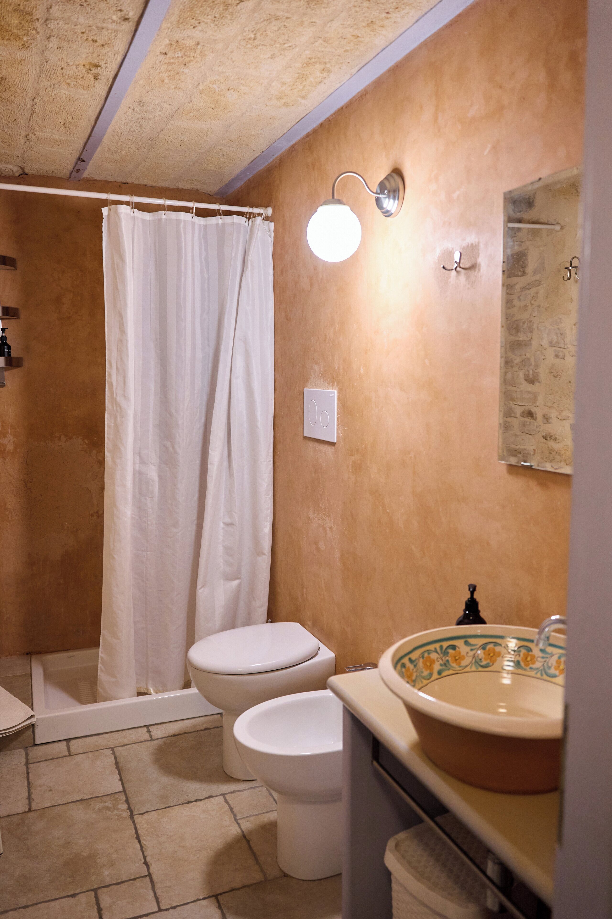 A bathroom with a shower, two toilets, a sink, and a light fixture.