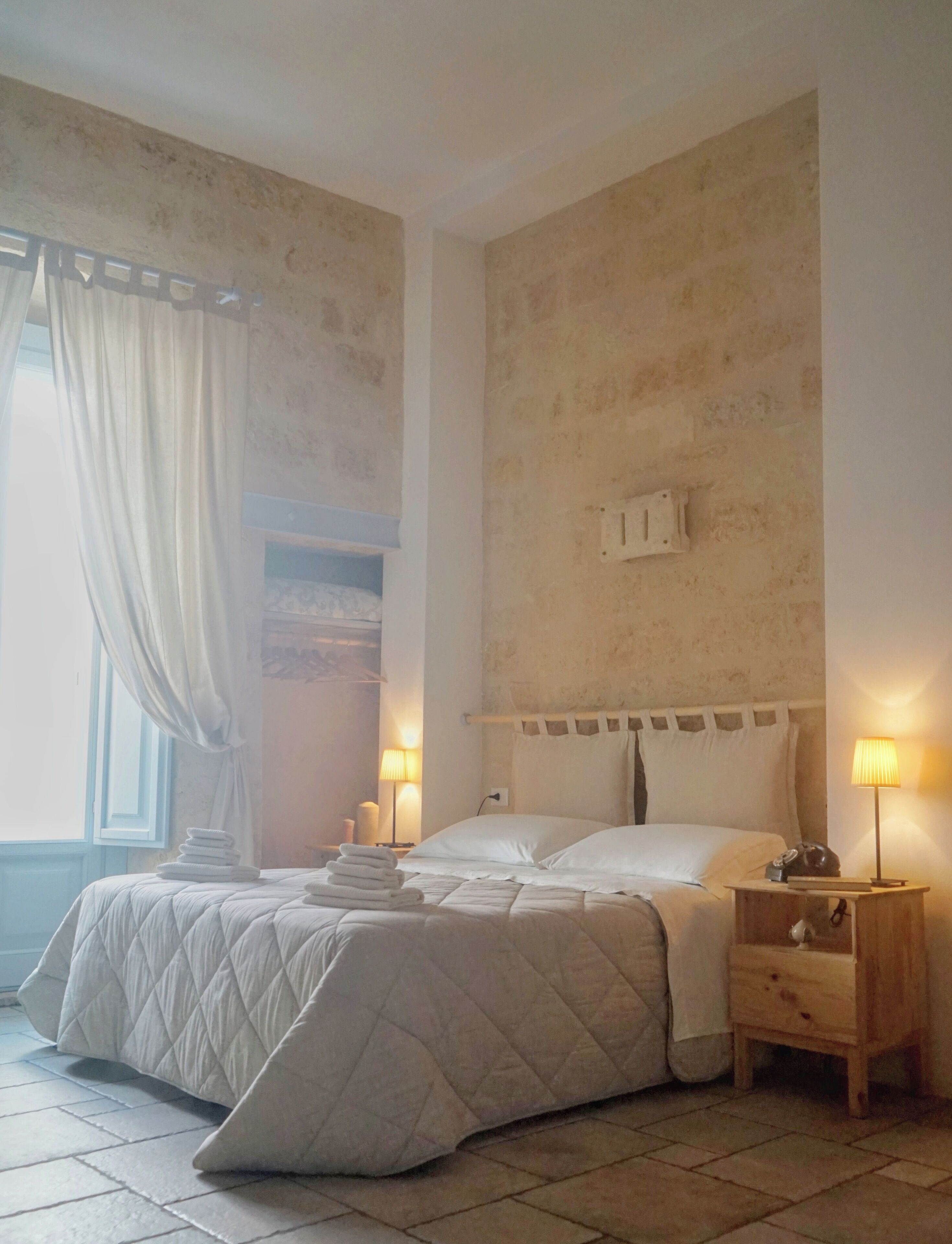A bedroom with a bed, nightstands, a lamp, and a window with curtains.