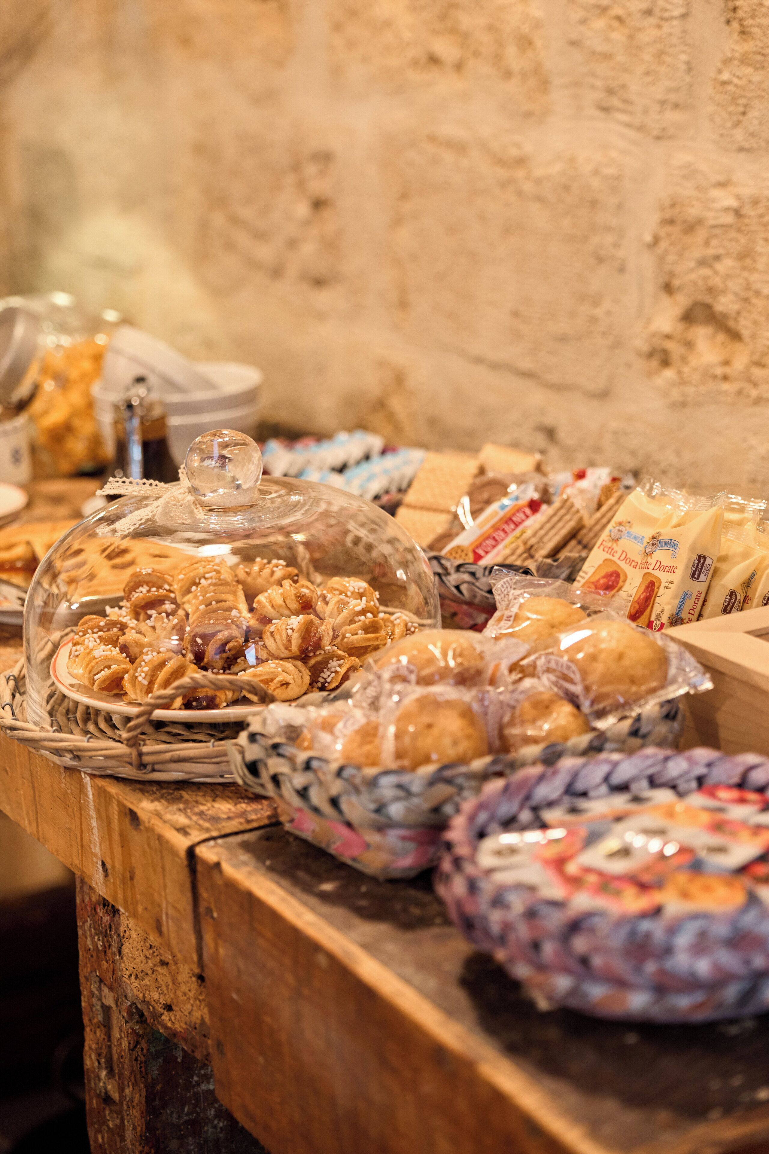Una mesa de buffet con diversas opciones de panadería y pastelería, como pan, bollos y pasteles, cubiertos con campanas de cristal.