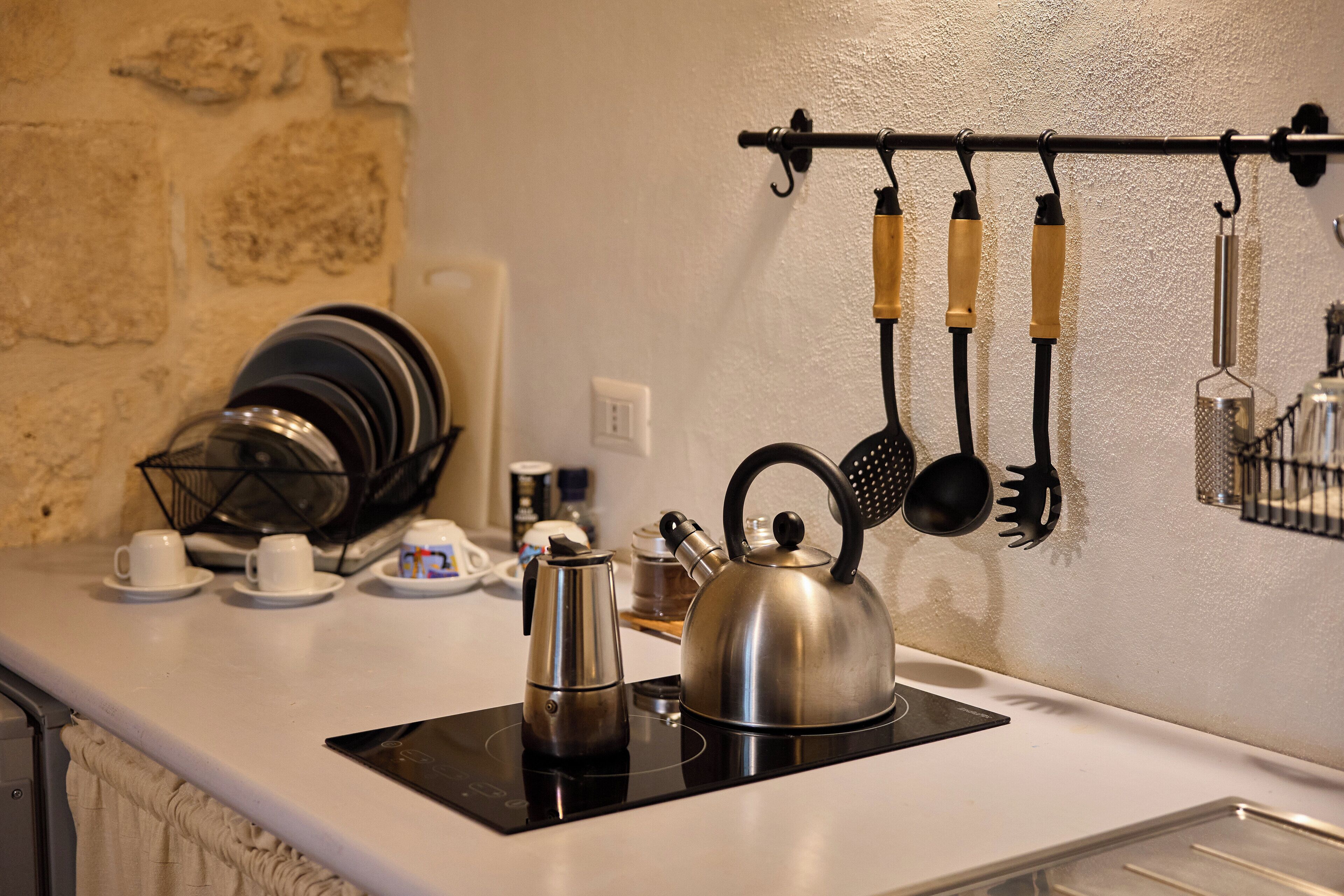 A kitchen with a stove, kettle, and various utensils hanging on the wall.