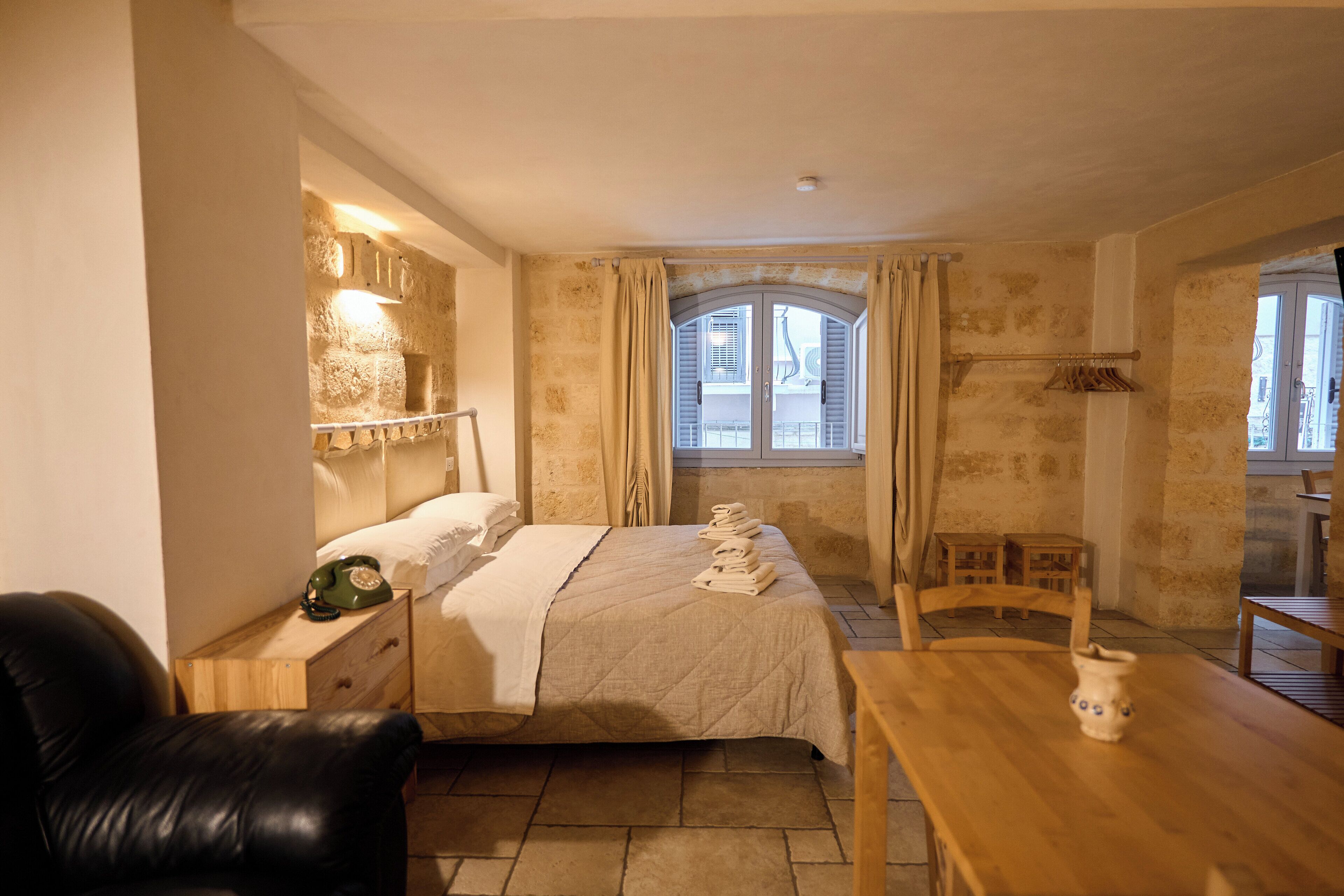 A bedroom with a bed, bedside table, lamp, and a view of the outside through a window.