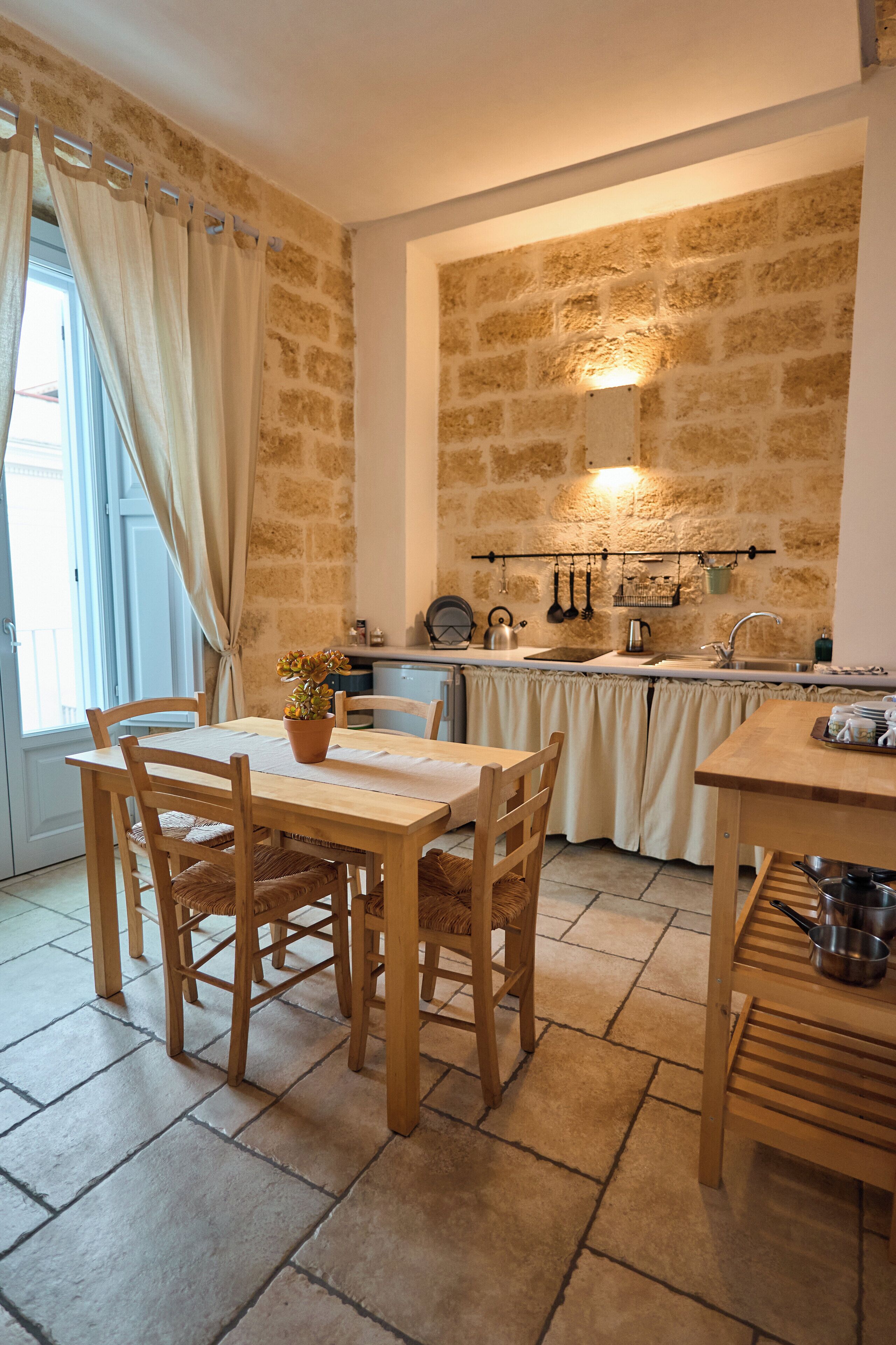 A cozy kitchen with stone walls, wooden furniture, and a small dining area.