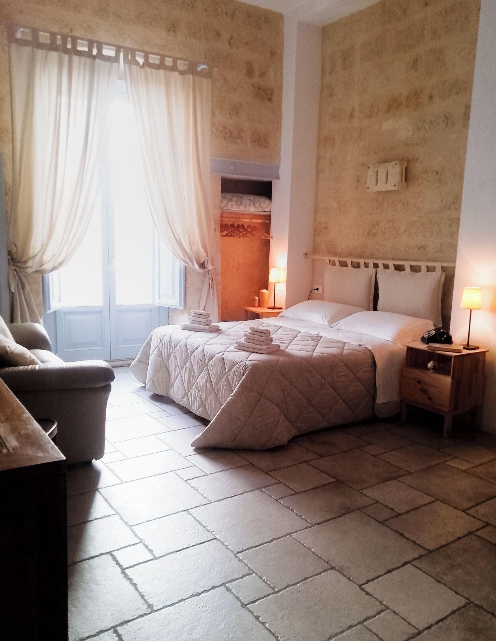 A hotel room with a bed, a chair, a nightstand, and a window with curtains.
