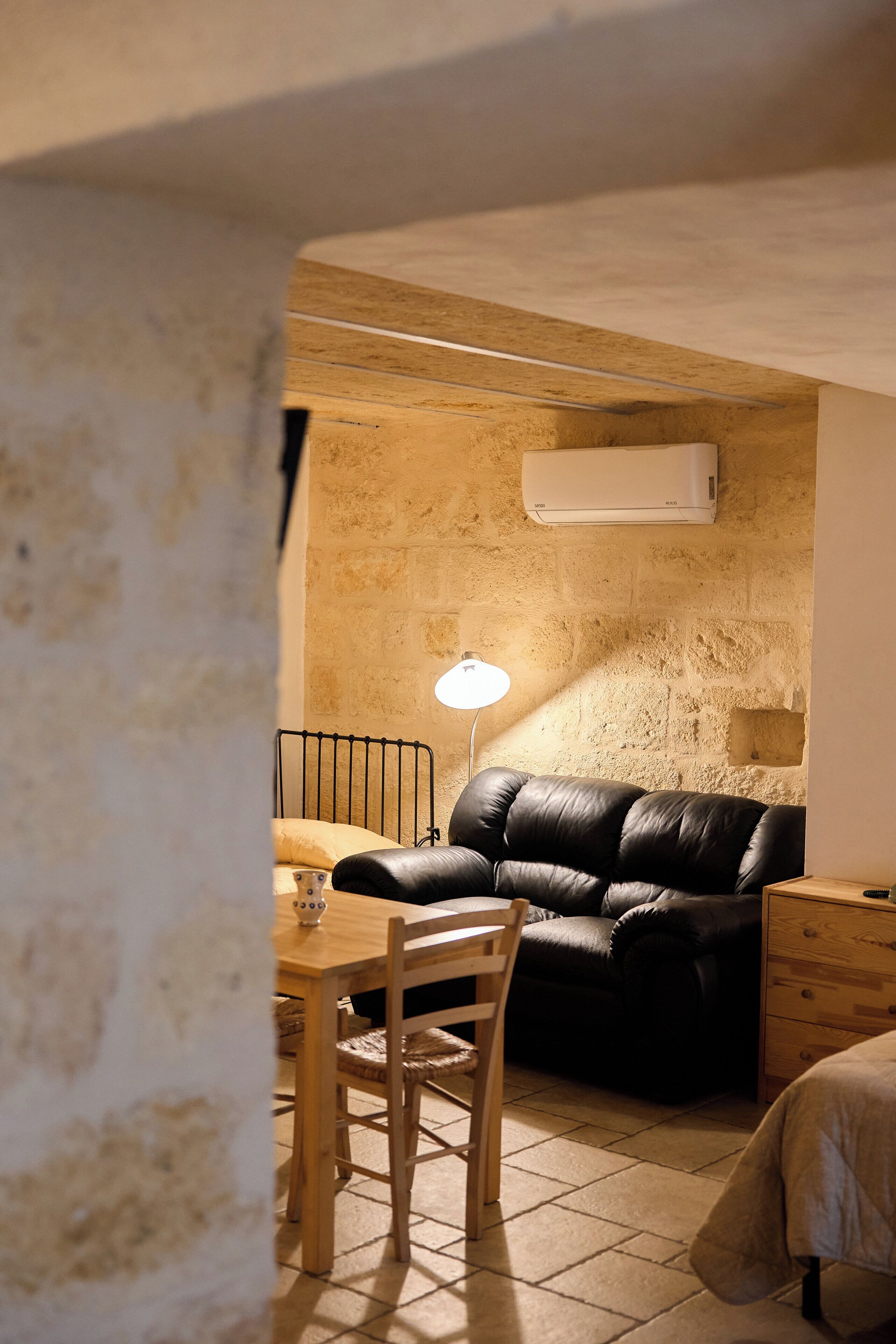 Um quarto acolhedor com um sofá de couro preto, uma mesa de jantar de madeira com cadeiras e uma mesa de cabeceira com abajur.