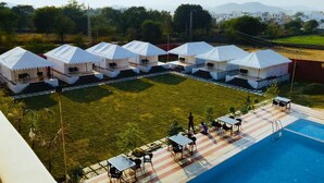 A hotel with multiple white tents, a swimming pool, and outdoor seating. - Dreams Resort Udaipur (Udaipur)